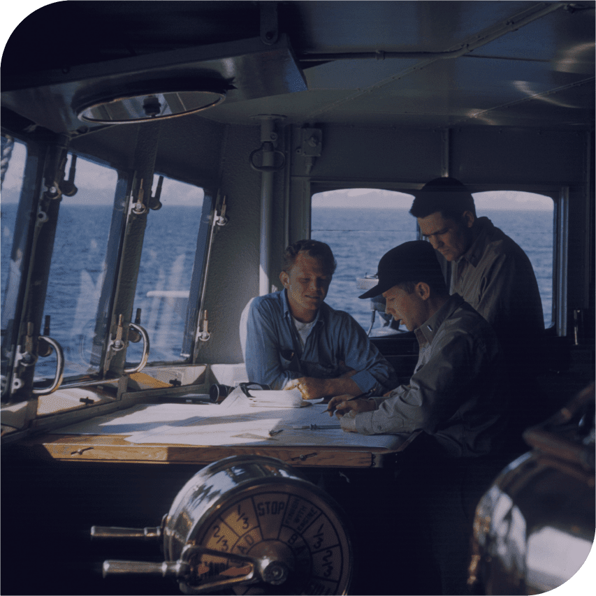 Sailors planning their course collaboratively over several charts.